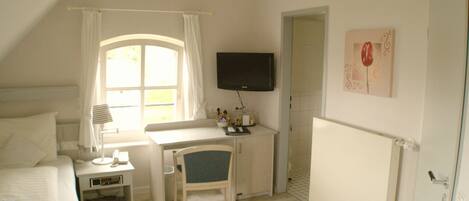 Une chambre à coucher avec un lit, un bureau, une chaise, un téléviseur et une fenêtre avec des rideaux.