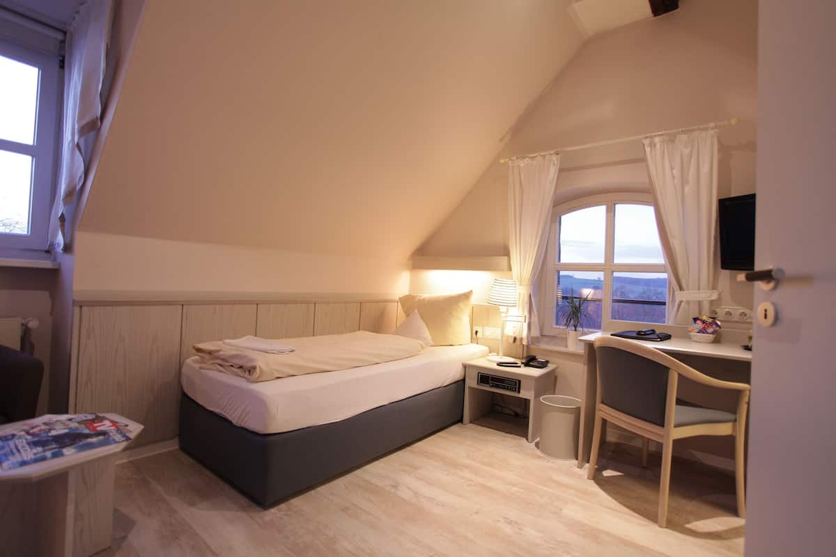 A bedroom with a bed, bedside table, chair, desk, and a window with curtains.
