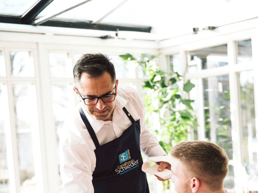 A waiter serving a meal to a customer in a well-lit restaurant with large windows and indoor plants.