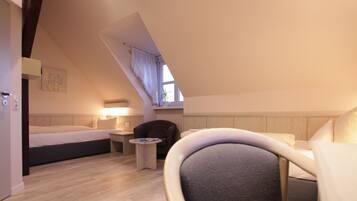 A cozy, well-lit room with a bed, a chair, a small table, and a window with curtains.