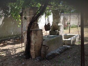 Un entorno rústico al aire libre con una estructura de piedra, una cesta colgante y un cubo de metal.