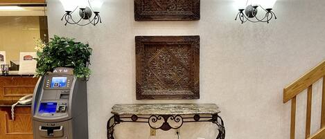 An ATM, two ornate wall-mounted light fixtures, and a decorative table with a menu stand in a lobby area.