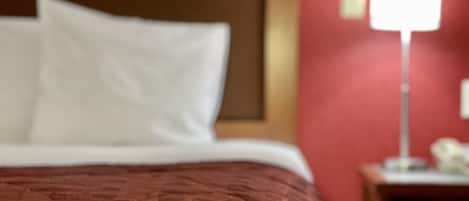 A bed with a patterned cover and white pillows, a red wall, and a bedside table with a lamp.
