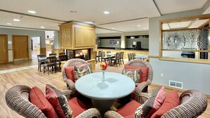 A spacious living area with a round table, wicker furniture, and a fireplace. - FairBridge Inn & Suites Fort Wayne (Fort Wayne)