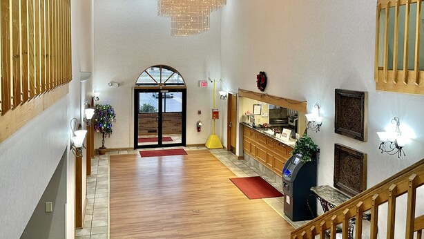 A spacious lobby with a wooden floor, a large chandelier, a reception desk, and a view of the parking area through a glass door. - FairBridge Inn & Suites Fort Wayne (Fort Wayne)