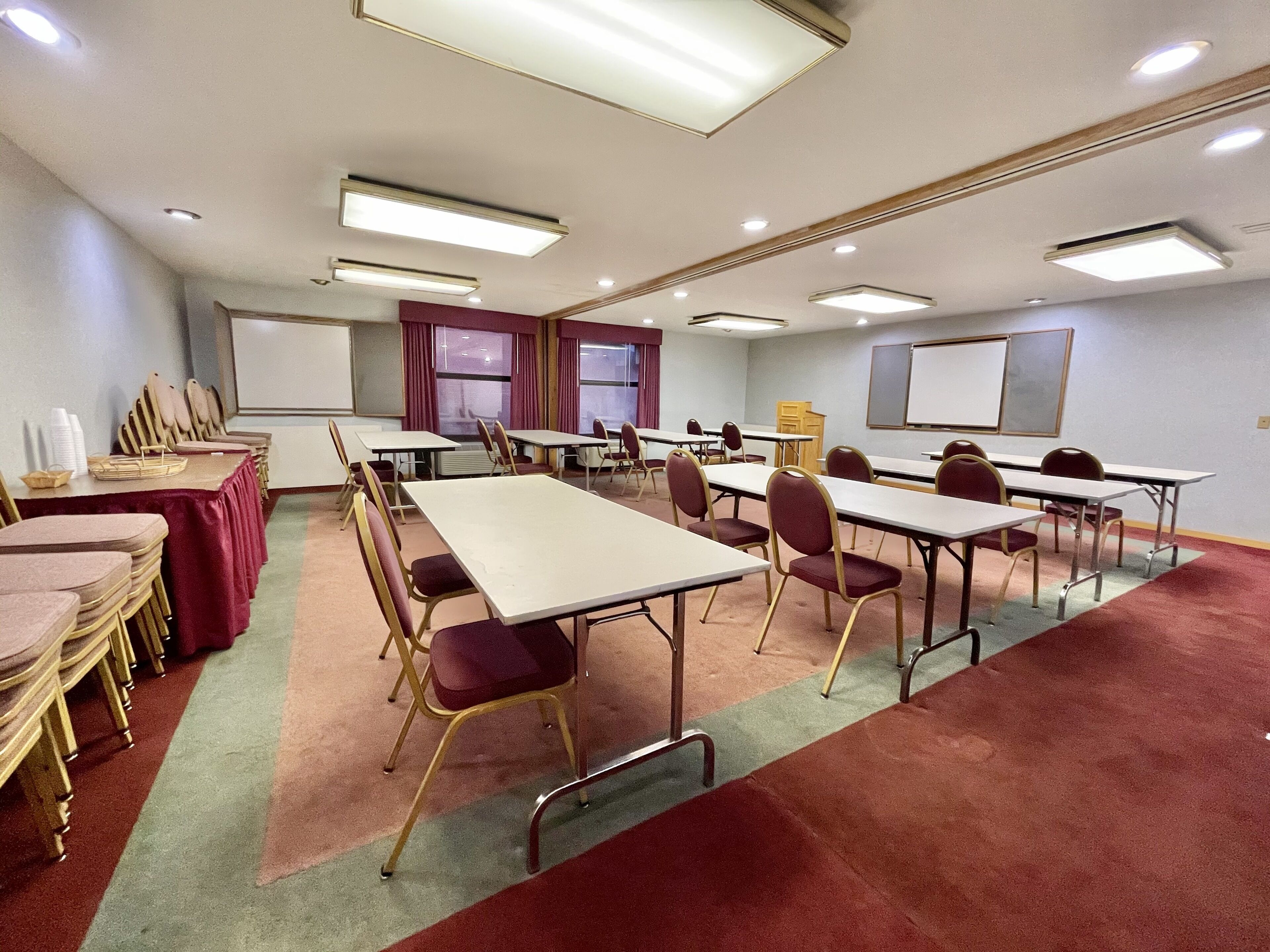 Un salón de conferencias con varias mesas y sillas, una pantalla de proyector y suelo alfombrado.