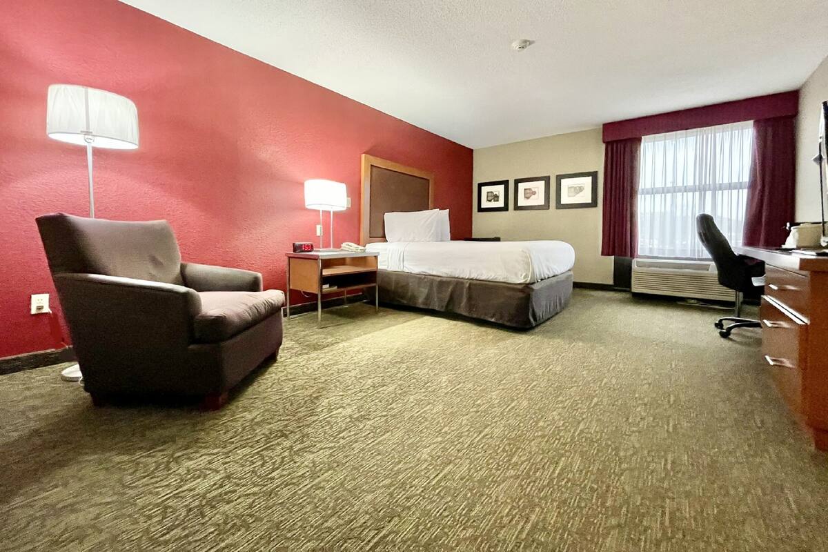 A hotel room with a bed, a desk, a chair, a lamp, and a window with curtains.
