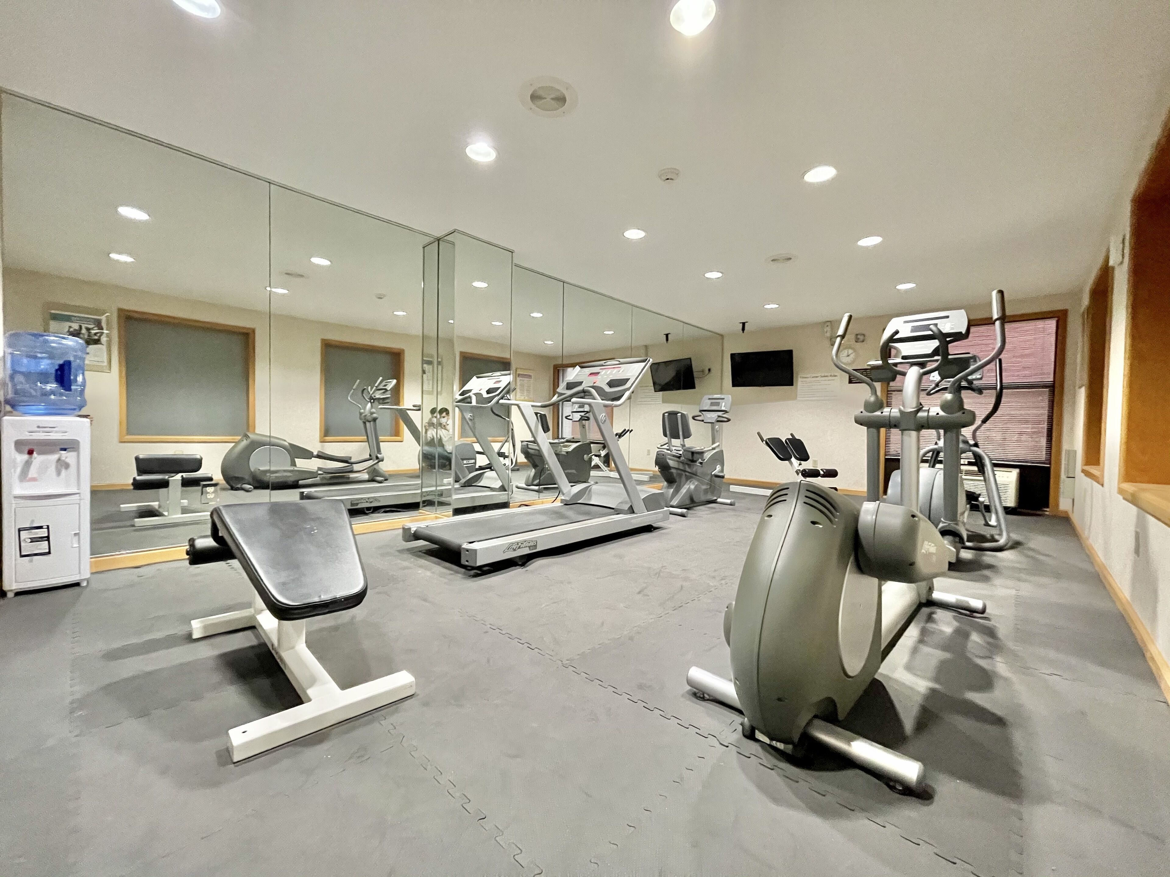 A gym with various exercise equipment, a water dispenser, and a large mirror.