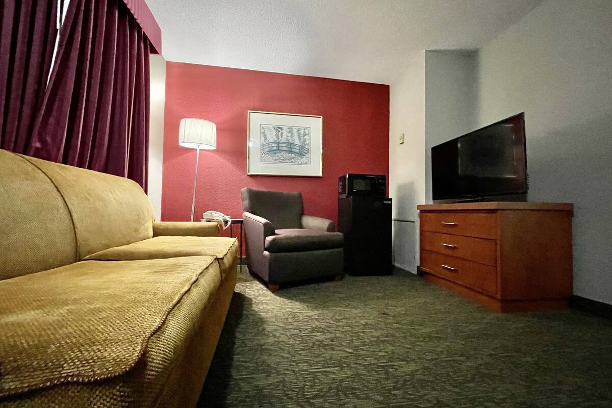 A hotel room with a sofa, armchair, television, and a refrigerator.