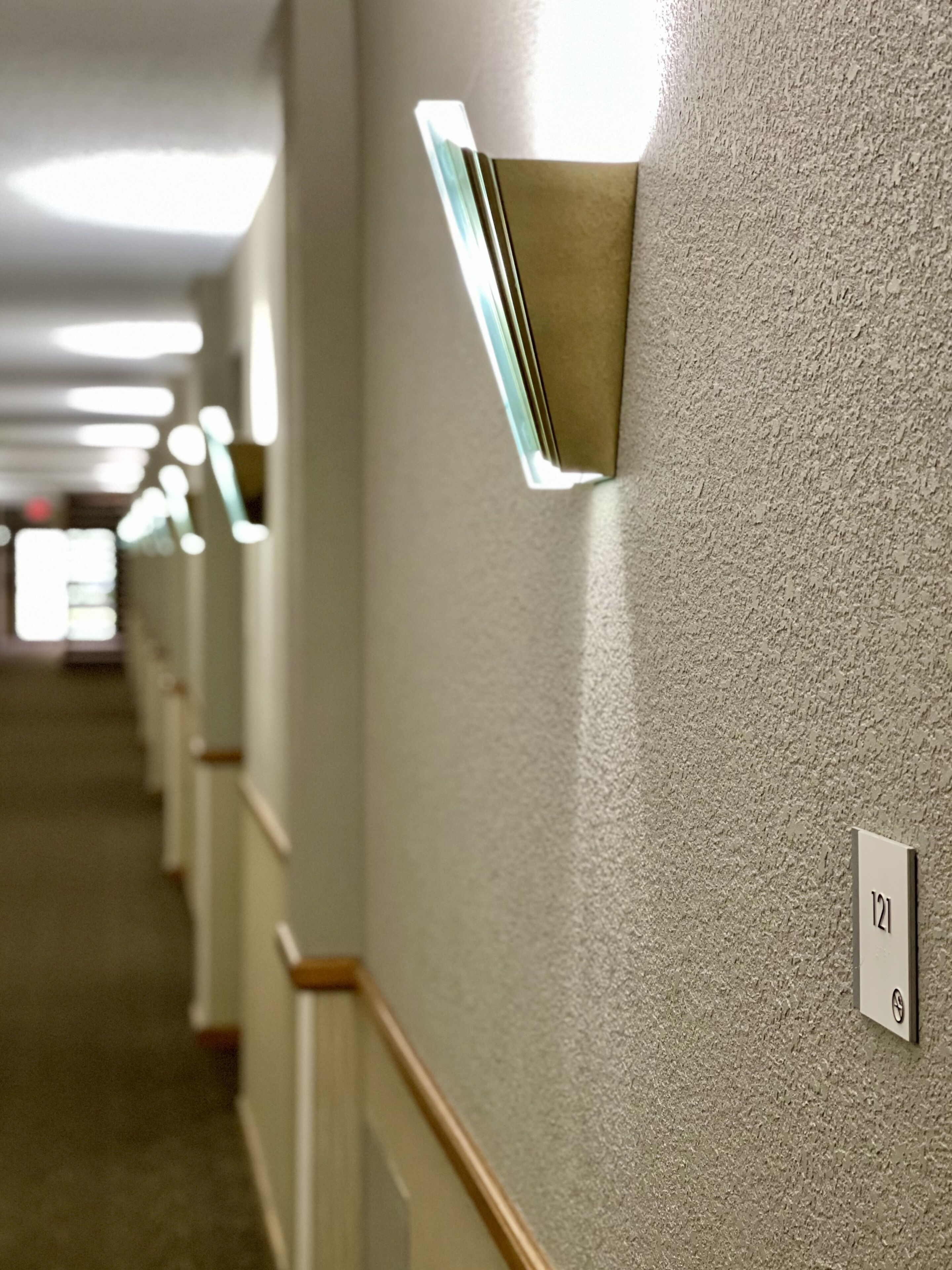 A hallway with a textured wall, a light fixture, and a door with the number 121.