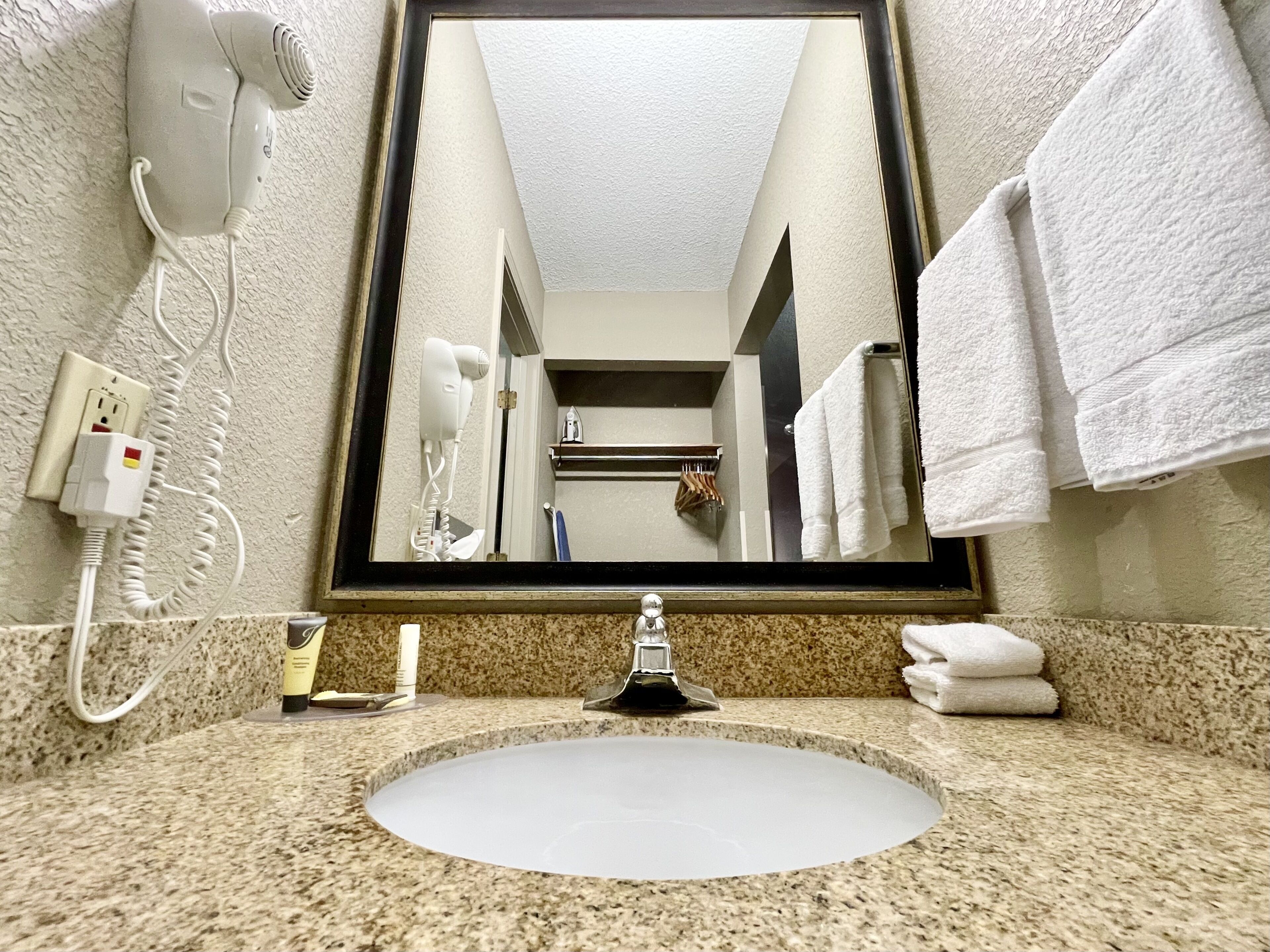 A bathroom with a sink, a hairdryer, a mirror, and towels.