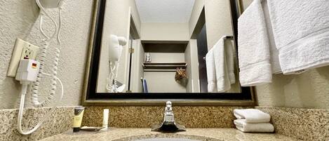A bathroom with a sink, a hairdryer, a mirror, and towels.