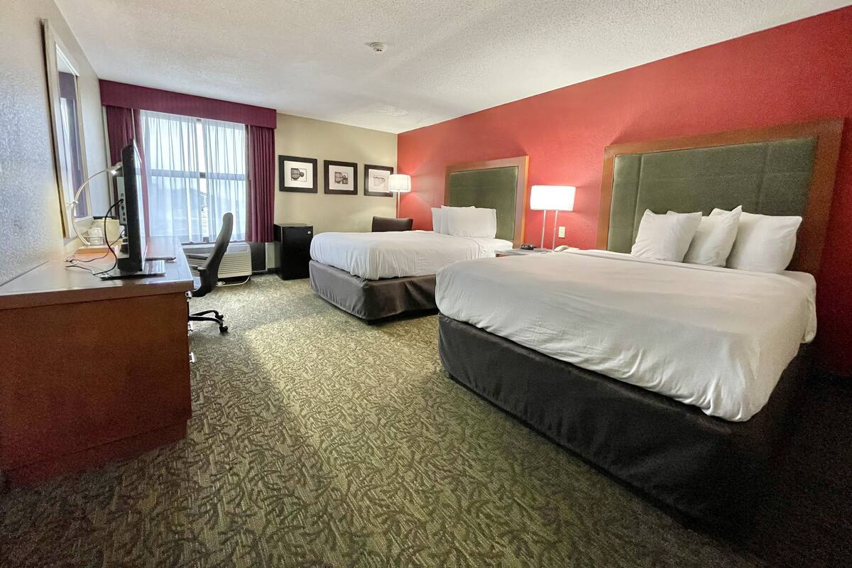 A hotel room with two beds, a desk, a chair, a lamp, and a window with curtains.