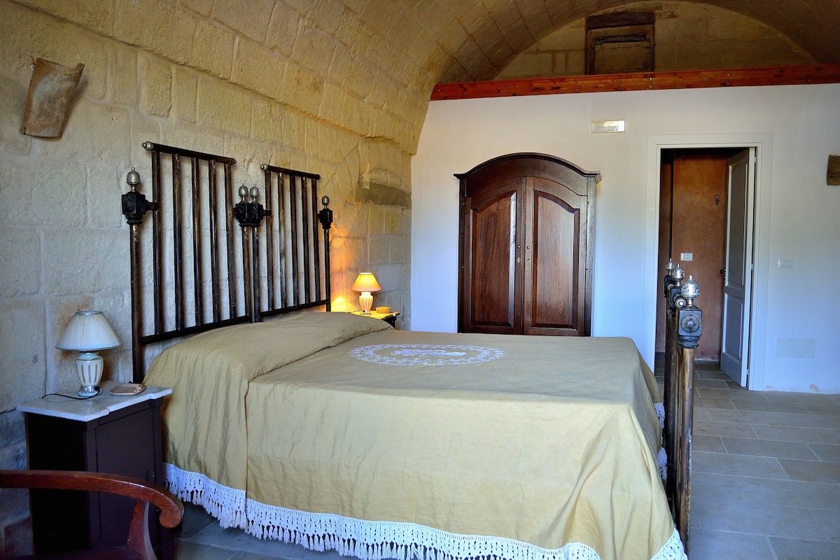 Une chambre à coucher avec un lit, une table de chevet, une lampe, une armoire en bois et un mur en pierre.