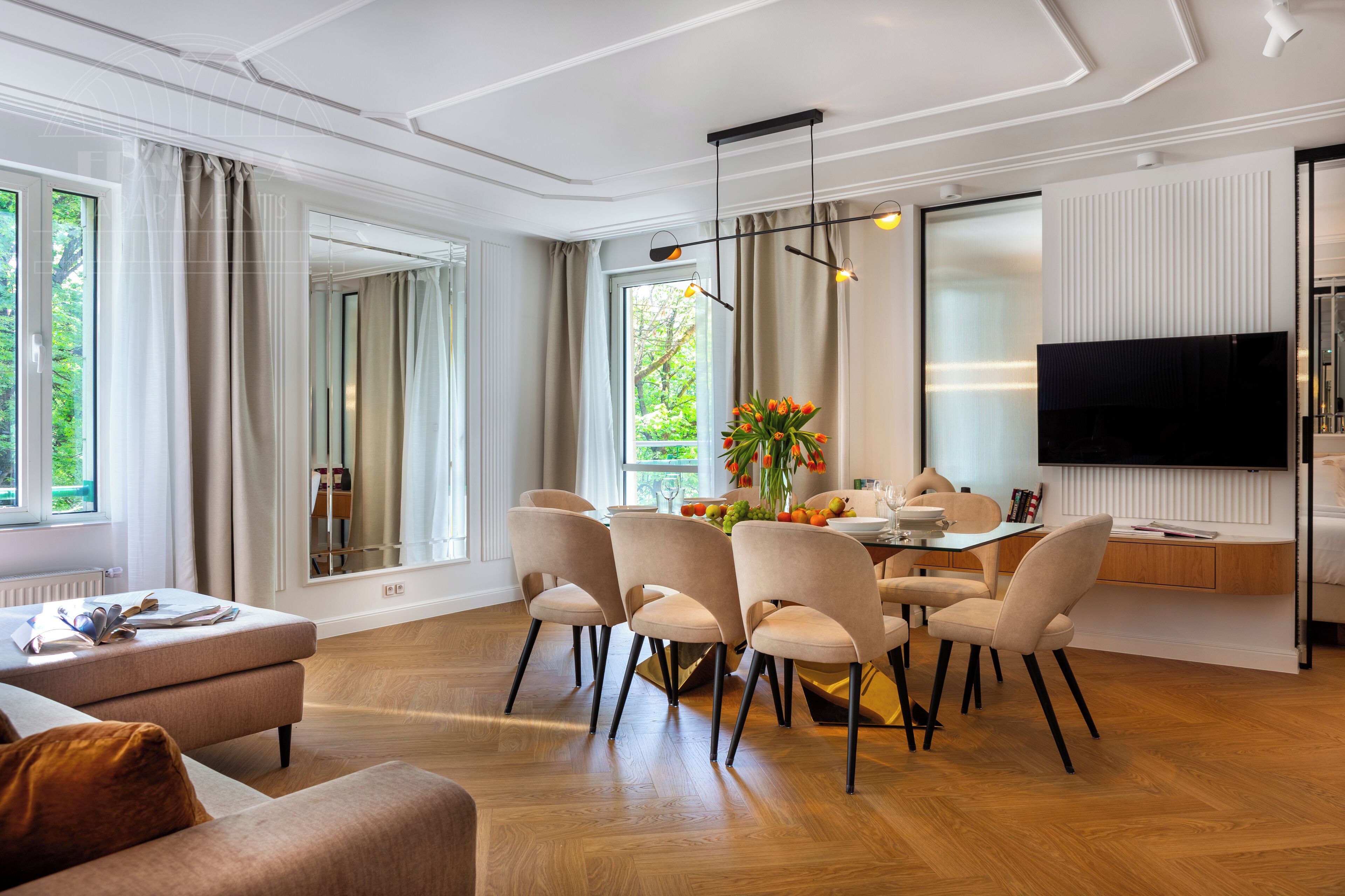 A modern dining area with a wooden table, beige chairs, and a TV mounted on the wall.