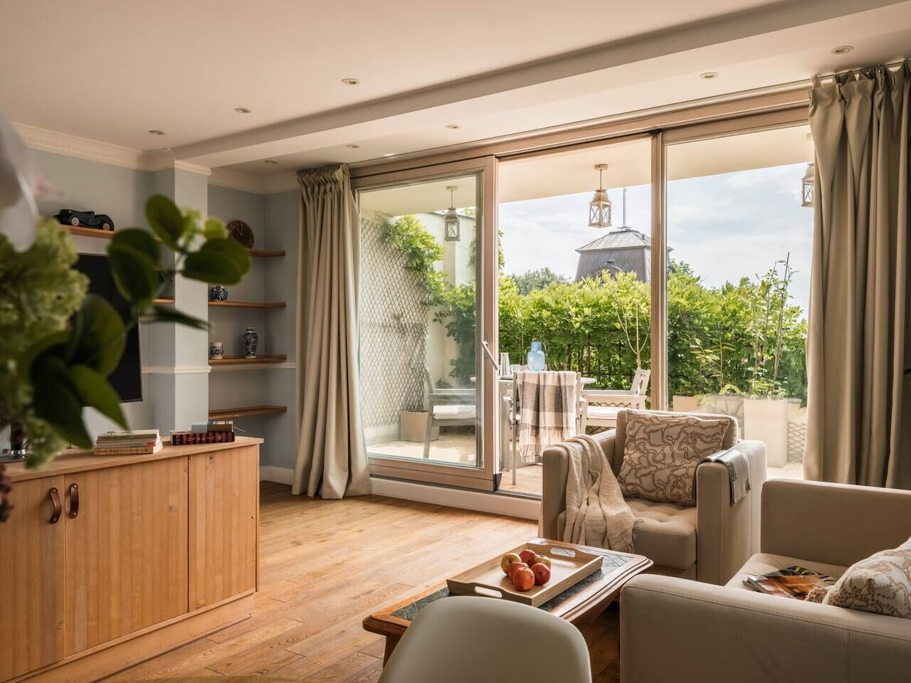 A modern living room with a sofa, a wooden cabinet, and a dining table with a tray of apples.