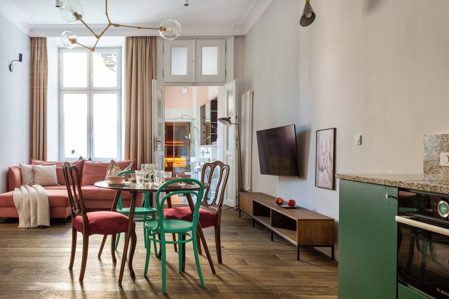 A modern living room with a sofa, dining table, chairs, a TV, and a kitchen area with a Bosch oven.