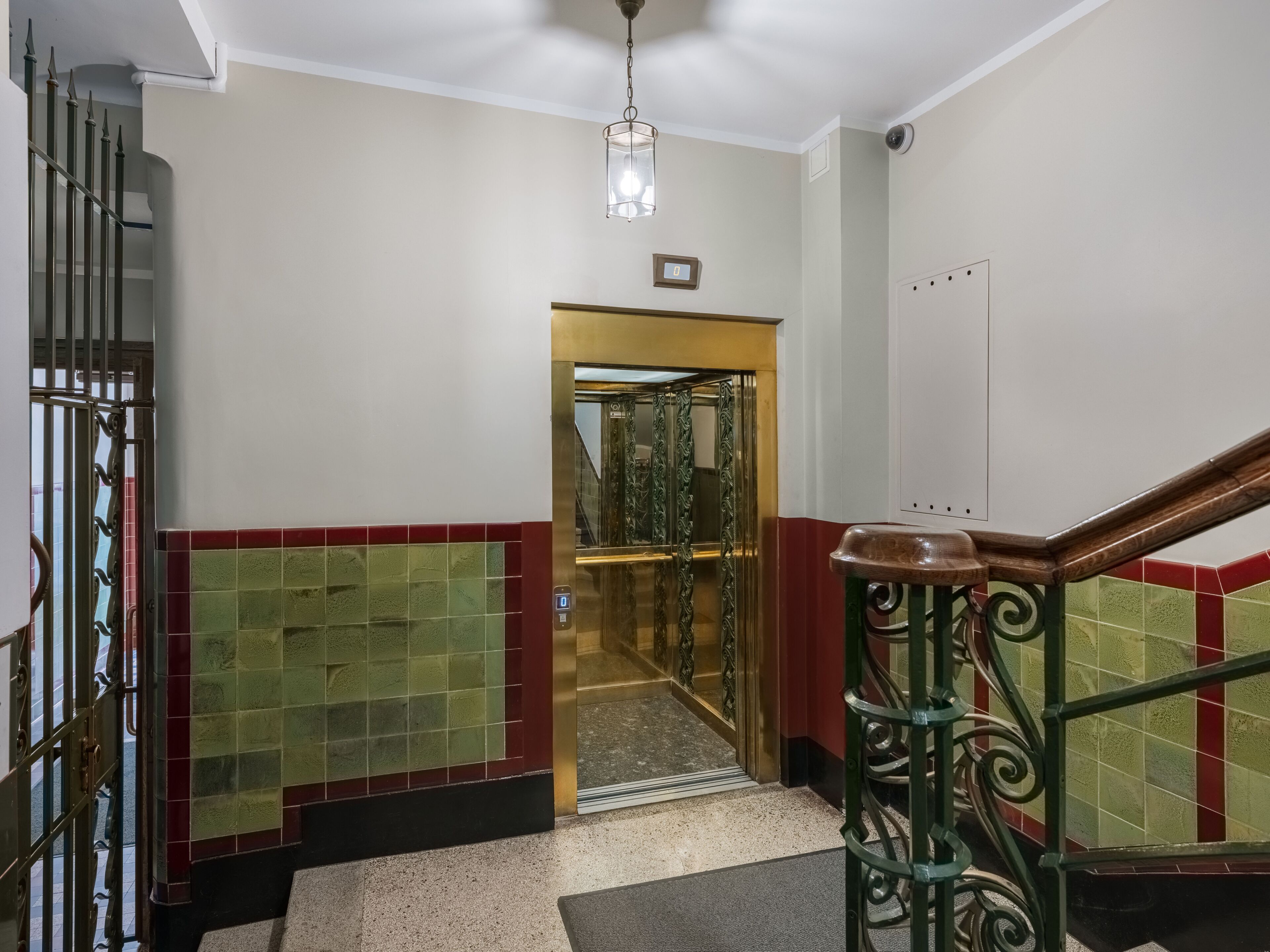 A staircase with a handrail, a glass elevator door, and a tiled wall with red and green tiles.