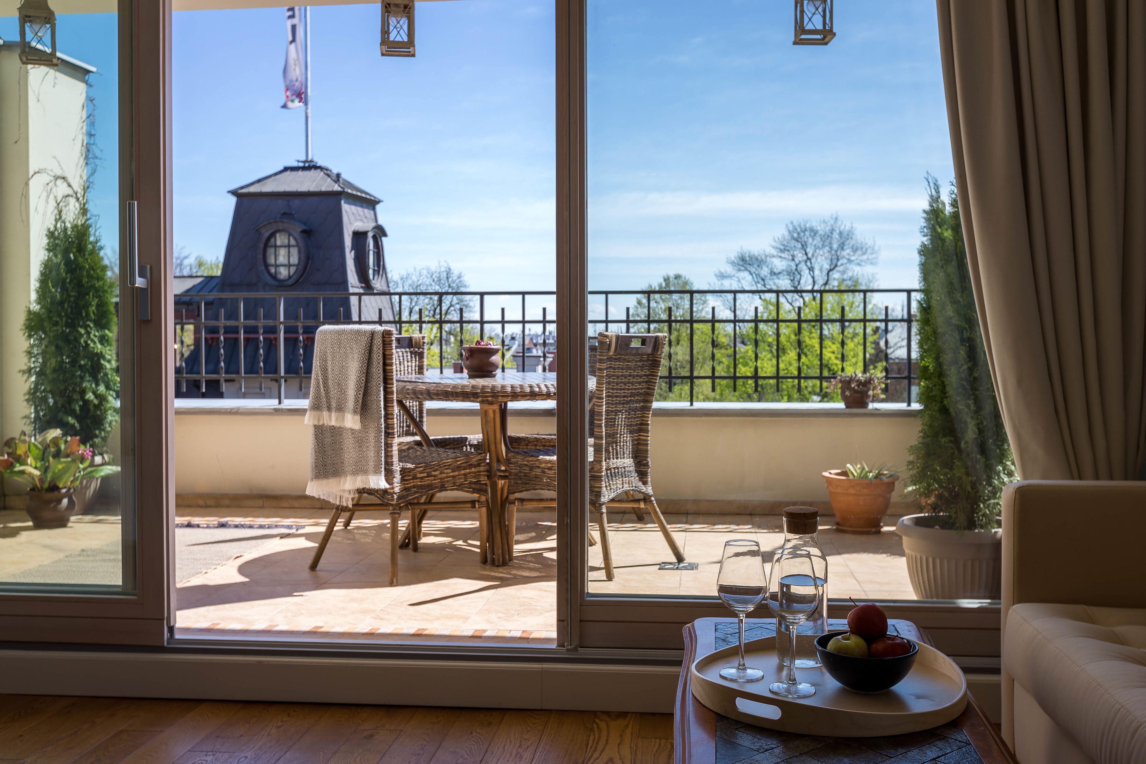 Un balcon agrémenté de meubles en osier, d’une table et d’un plateau sur lequel se trouvent un verre d’eau et des fruits.