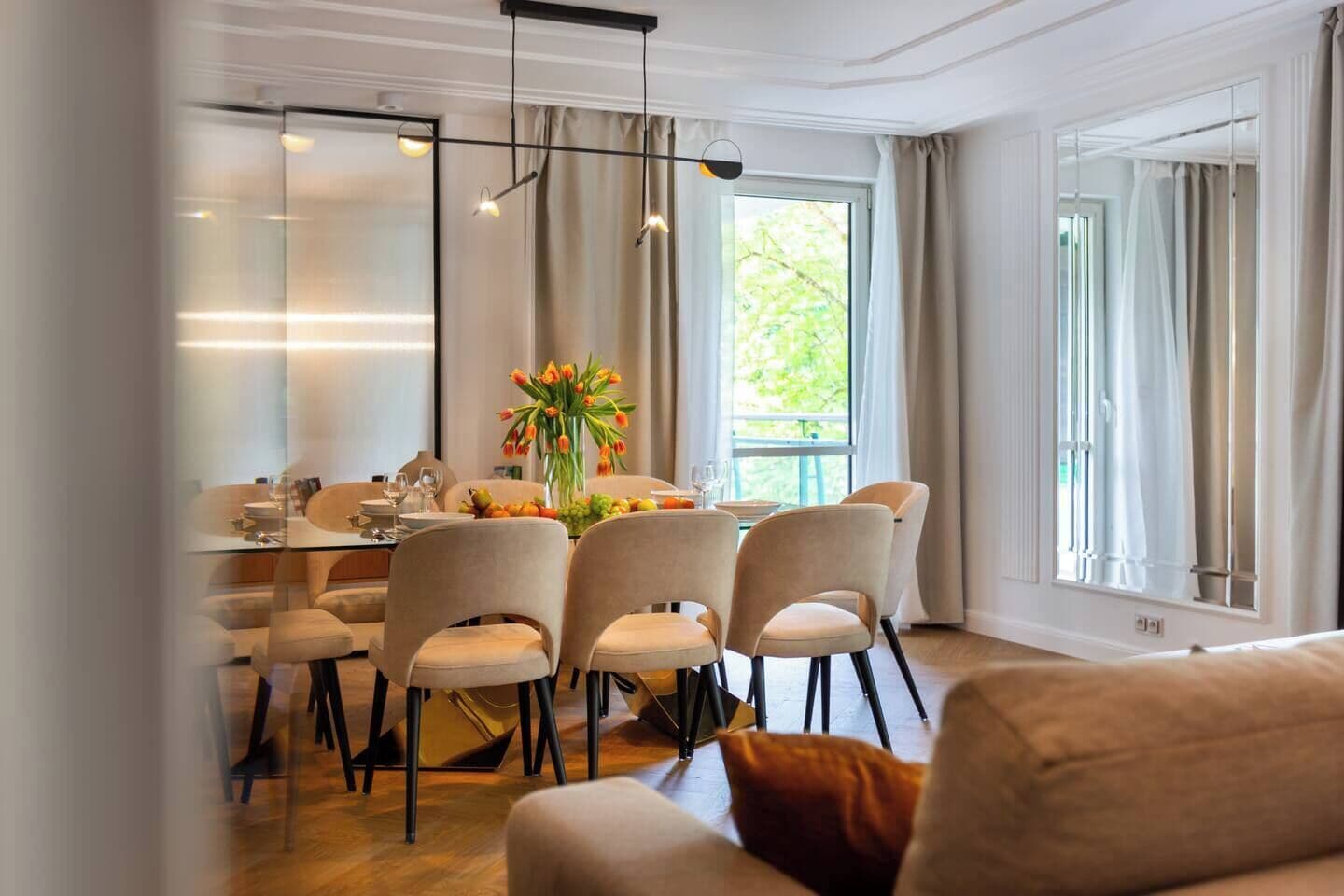 Een eetgedeelte met een glazen tafel, stoelen en een bloevas.
