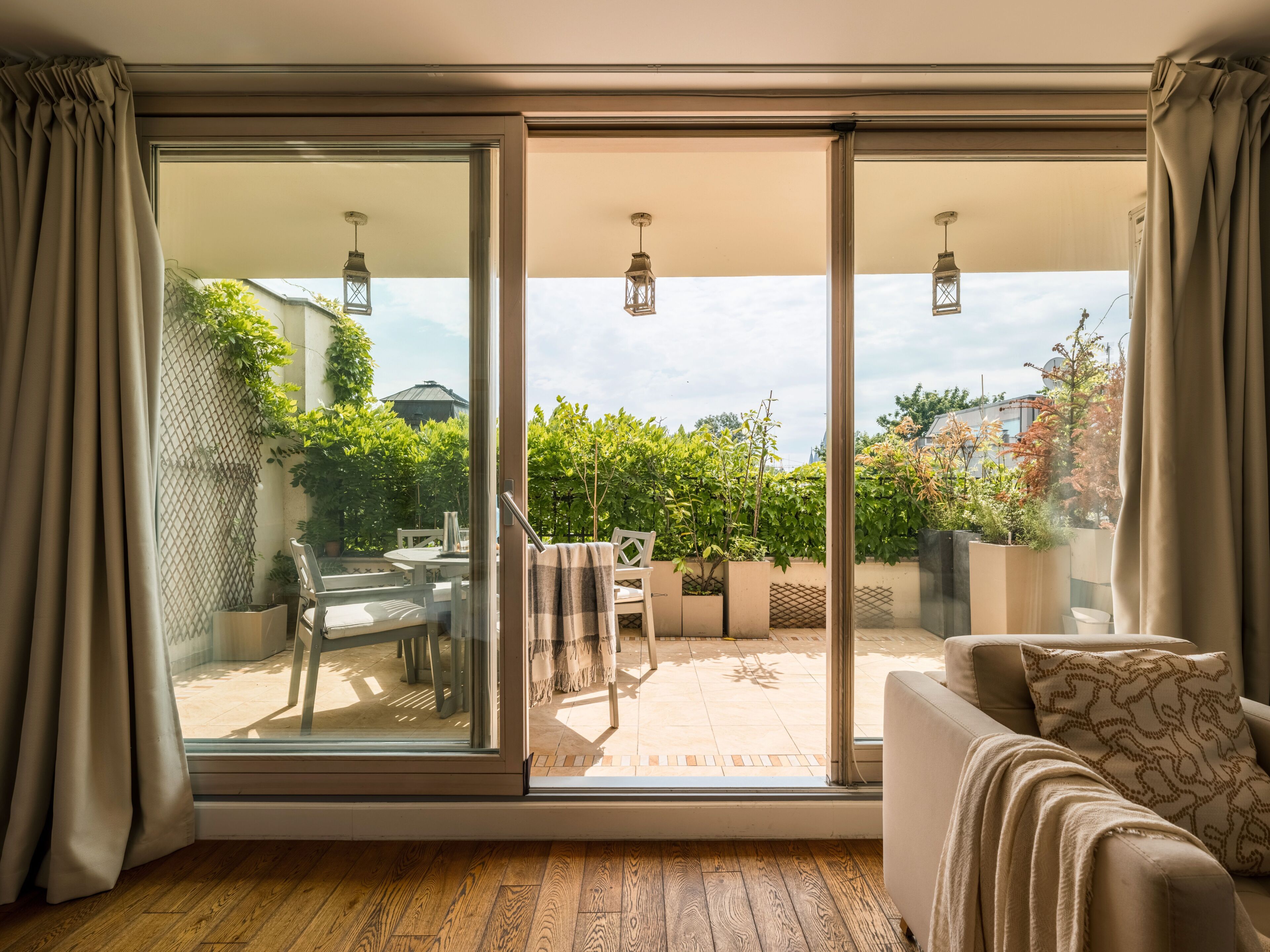 Una habitación con puerta corrediza de vidrio que da a un patio exterior, un sofá con cojines estampados y piso de madera.