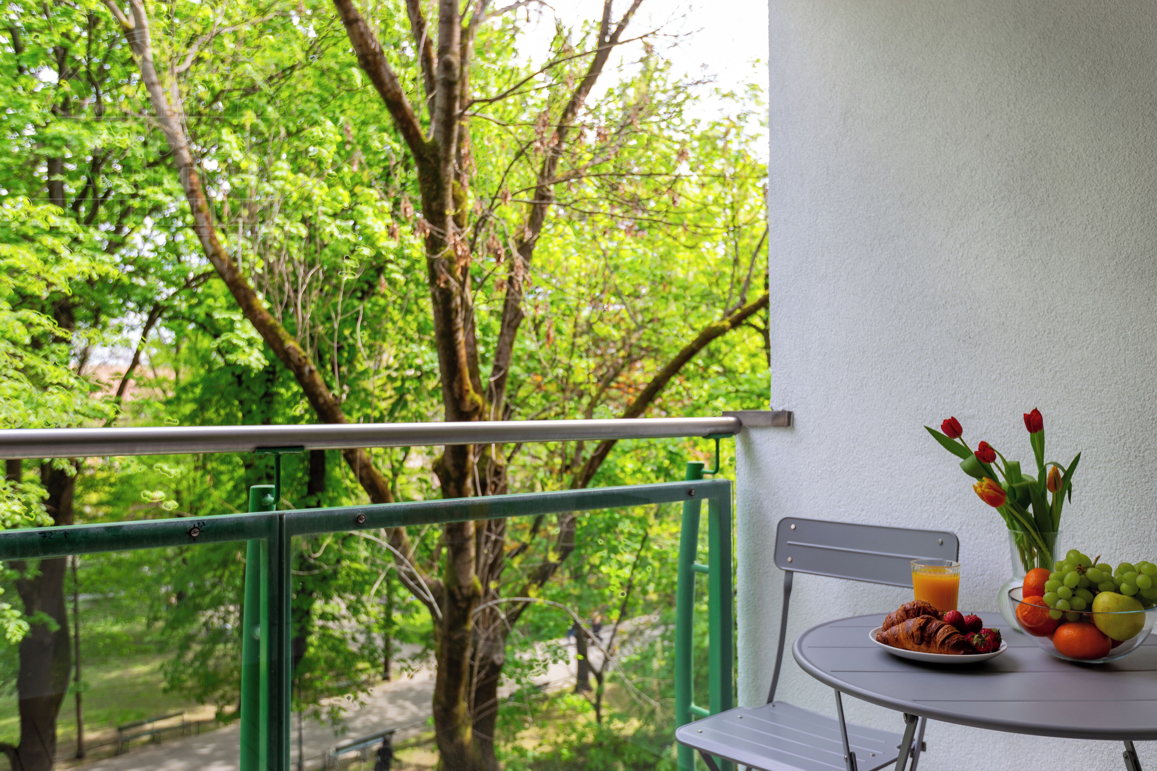 Een balkon met een ontbijttafel, compleet met croissants, fruit en een glas sinaasappelsap.