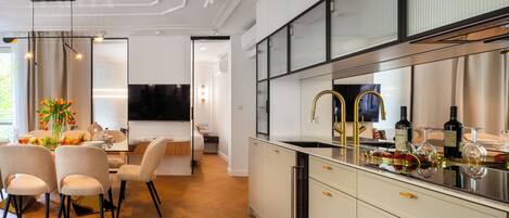 A modern kitchen with white cabinetry, a stainless steel sink, and a dining area with a table and chairs.