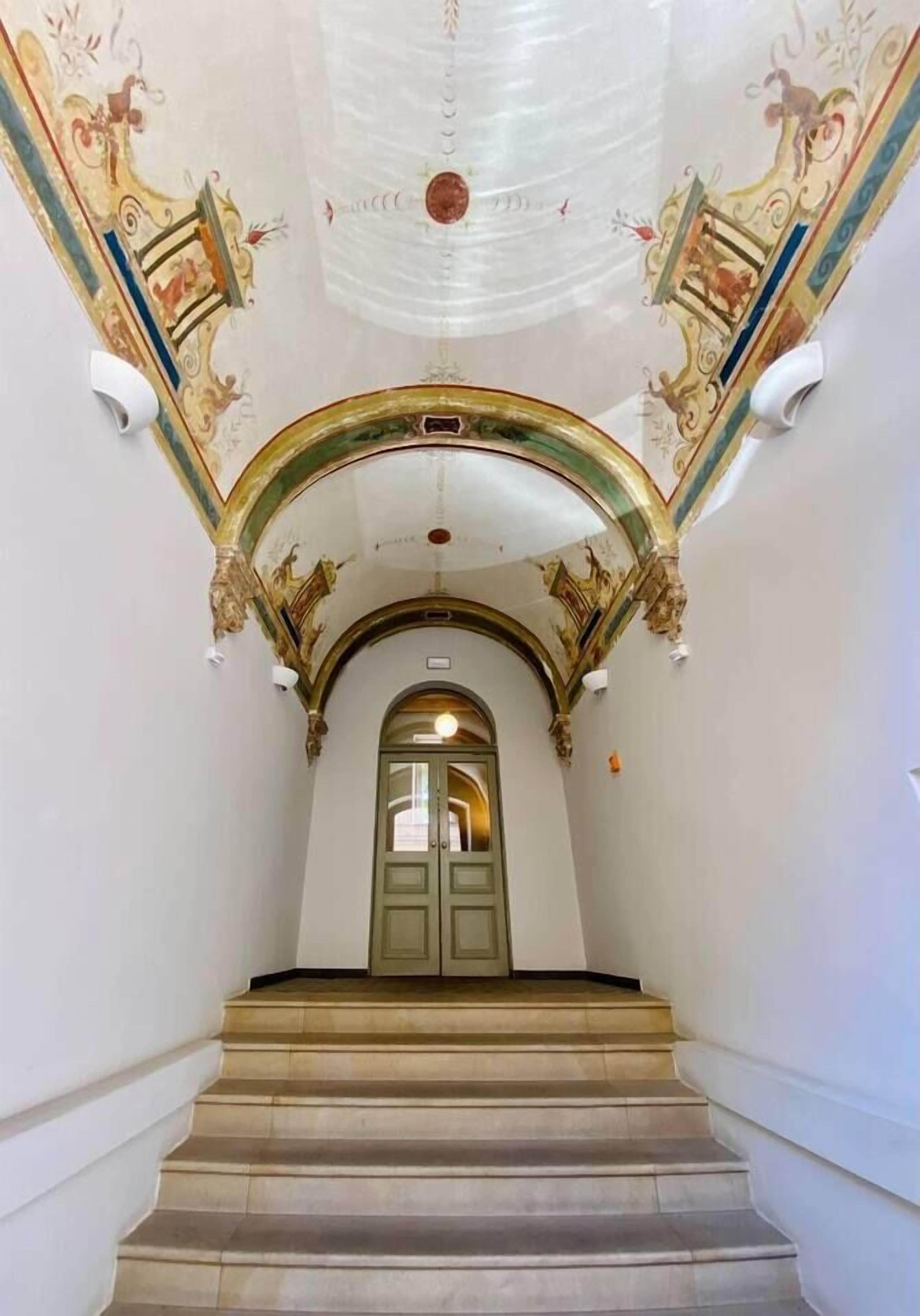 A grand staircase with ornate ceiling artwork and a green door at the top.