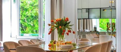 A modern dining area with a glass table, beige chairs, and a central vase with flowers.