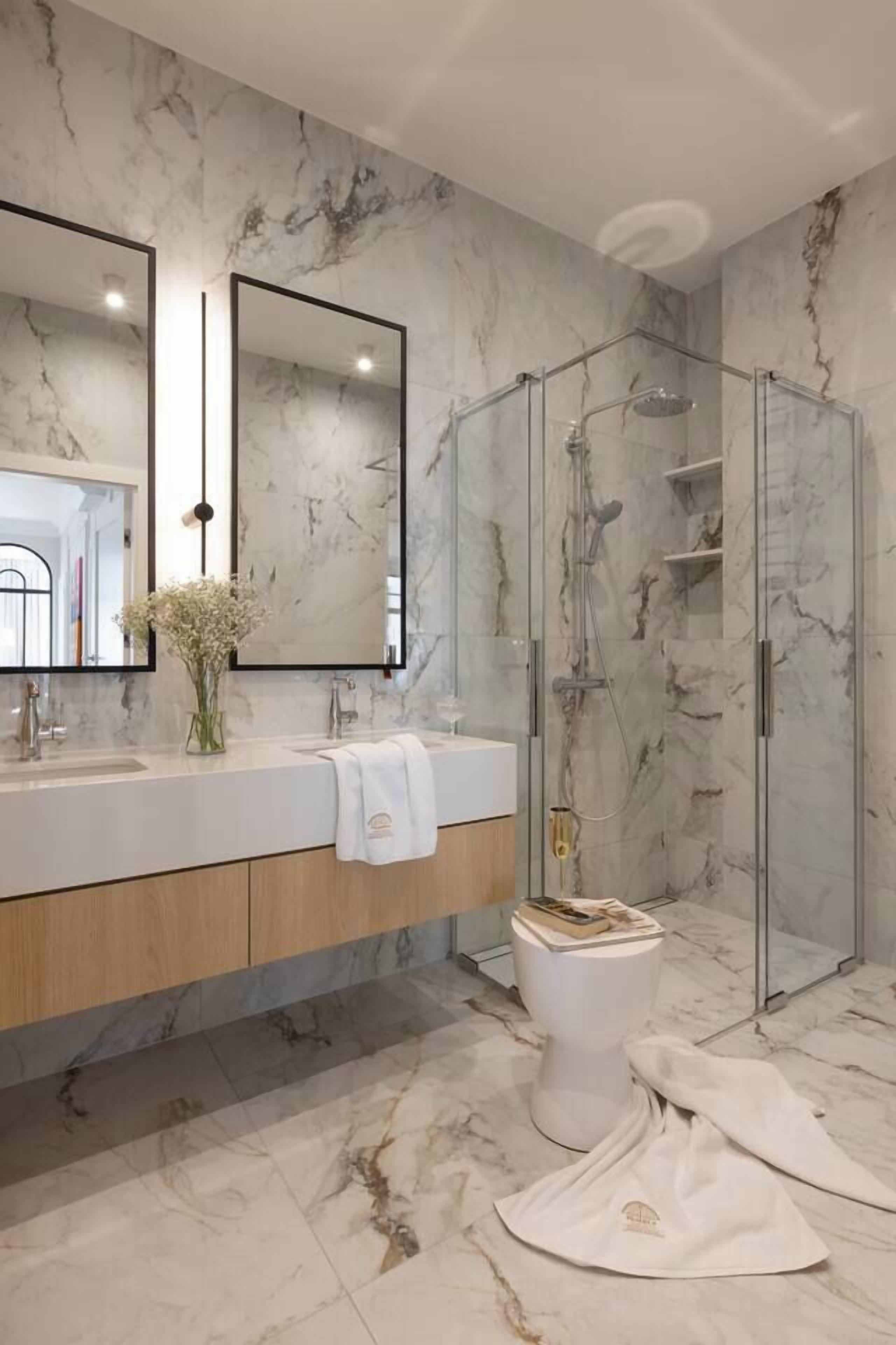 A bathroom with marble walls, a glass shower enclosure, a white sink with a towel, and a toilet.