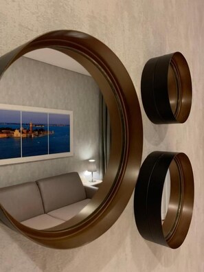 Un miroir rond offrant une vue sur le paysage urbain, un canapé et deux lampes fixées au mur.