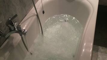 A bathtub with running water, a handheld showerhead, and a towel stack on a marble countertop.