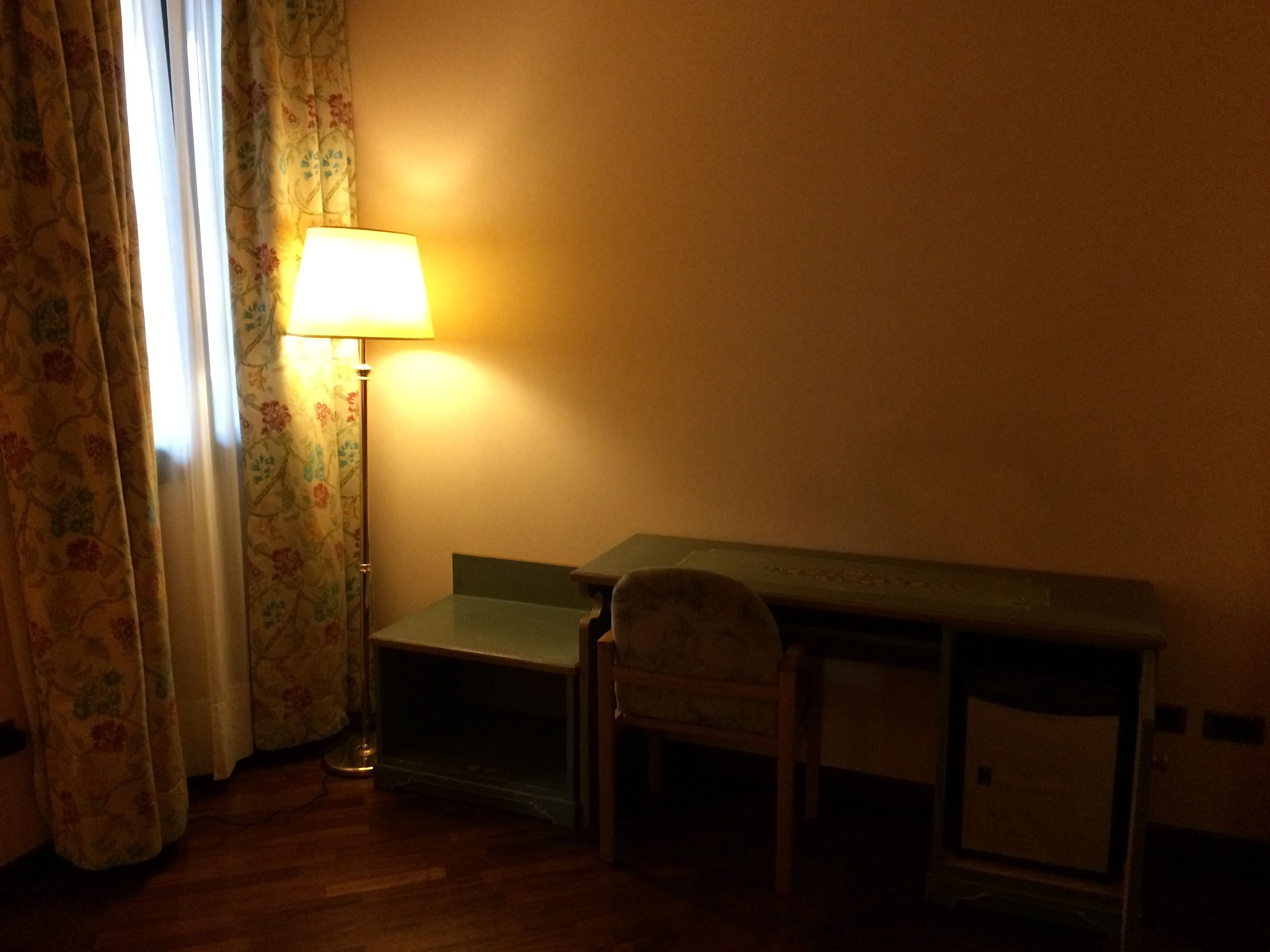 Una habitación con escritorio, silla, lámpara y cortinas estampadas.