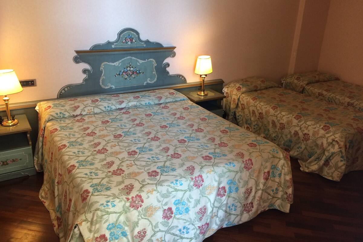 Ein Zimmer mit zwei Betten, jeweils mit blumigem Bettbezug, einem Holzkopfende und Nachttischlampen.