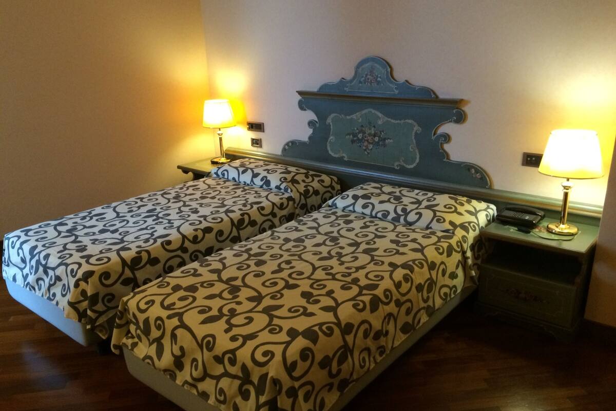 Ein Doppelbett mit gemusterten Betttextilien, ein Nachttisch mit Lampe und ein an der Wand befestigtes Telefon.