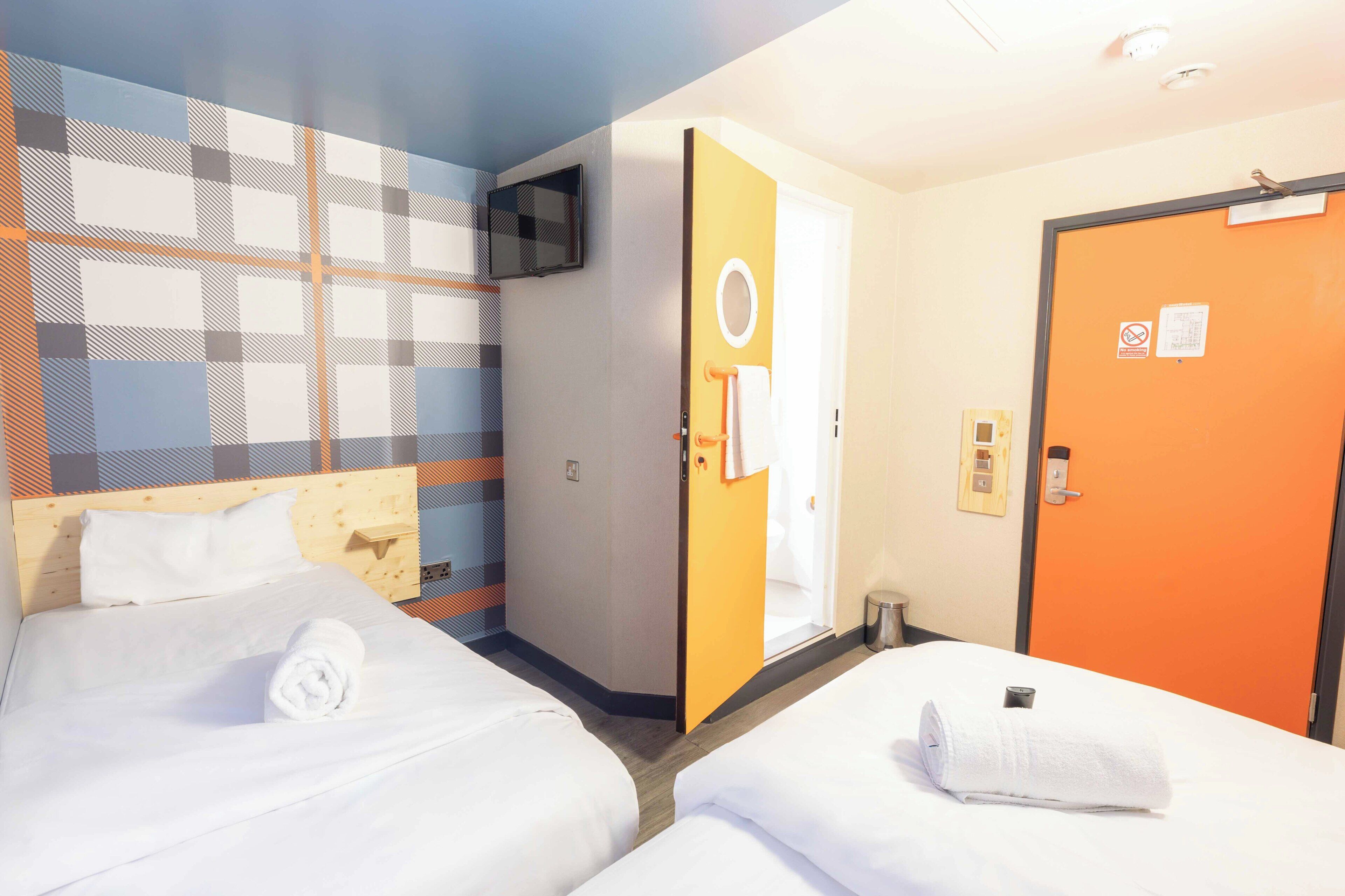 Habitación de hotel con dos camas, un televisor, una puerta con una toalla y una pared con un diseño geométrico.