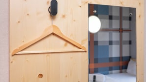A wooden door with a wooden hanger, a mirror reflecting a bed with a checkered headboard, and a small round light fixture above the mirror. - easyHotel Glasgow (Glasgow)