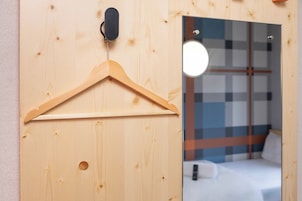 A wooden door with a wooden hanger, a mirror reflecting a bed with a checkered headboard, and a small round light fixture above the mirror.