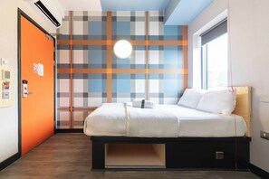 A hotel room with a bed, a wall-mounted air conditioner, a window, and a door.