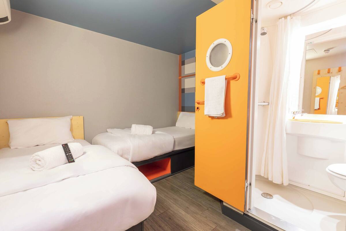 Een hotelkamer met twee bedden, een badkamer met douche en een spiegel aan de muur.