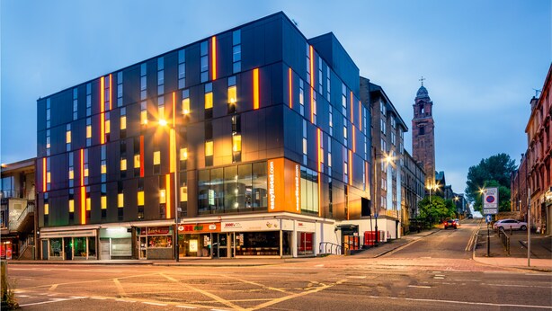 A modern hotel with a glass facade, a prominent tower in the background, and a street in front. - easyHotel Glasgow (Glasgow)