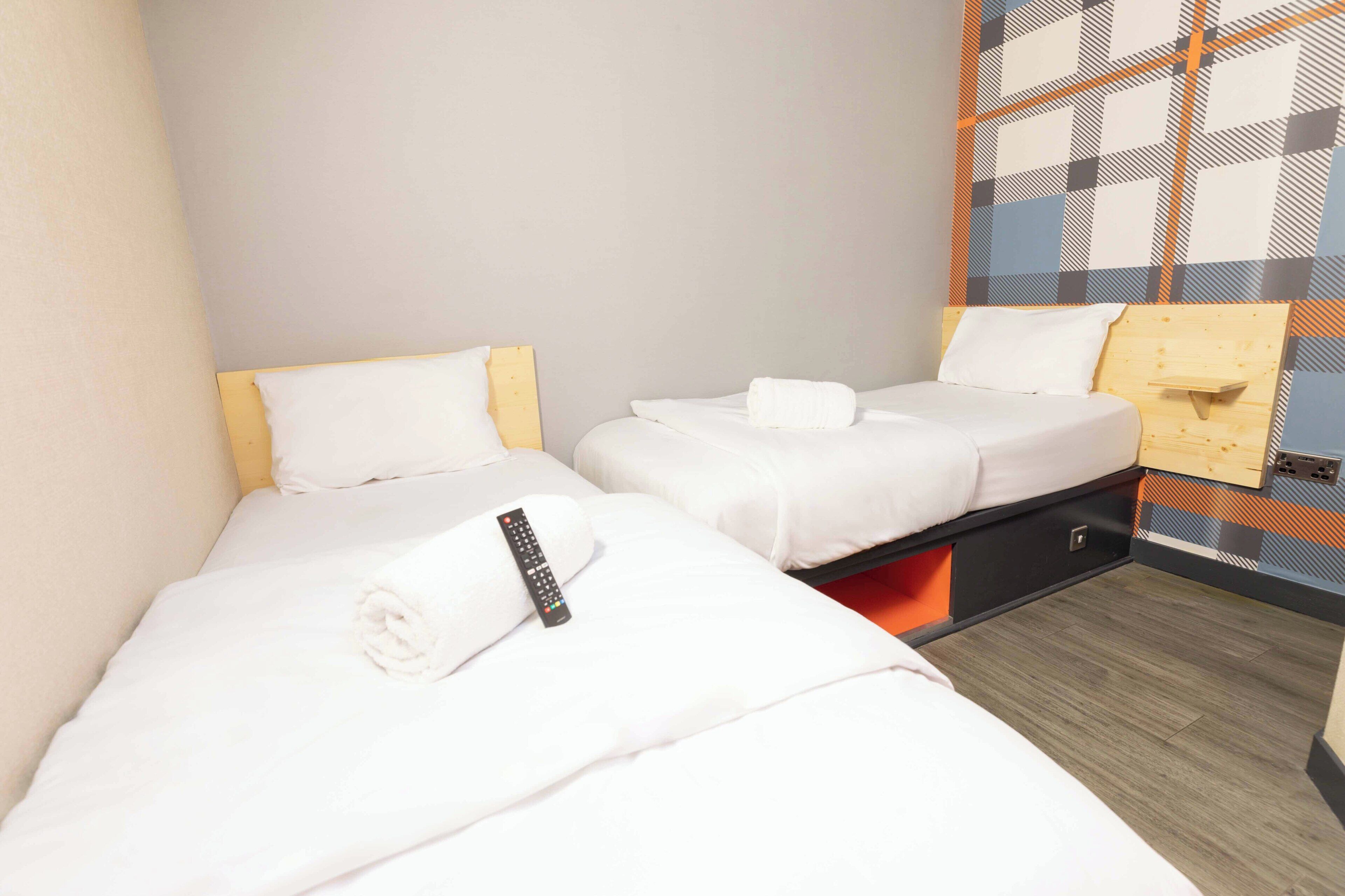 Ein kleines Hotelzimmer mit zwei Betten, einem Holzkopfende, einer Fernbedienung und einer Wand mit Muster.