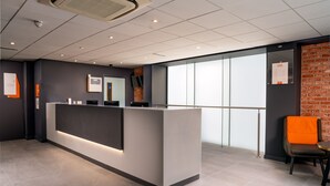 A reception area with a modern counter, a glass partition, and a brick wall. - easyHotel Glasgow (Glasgow)