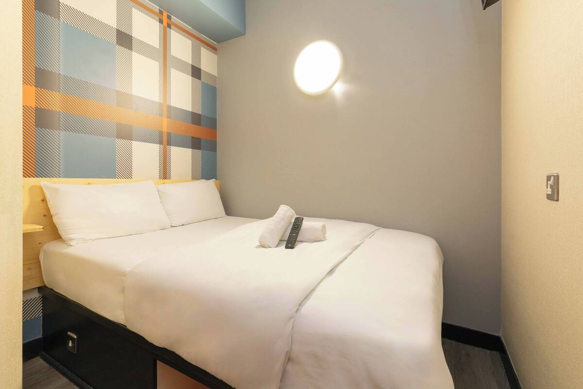 Een netjes opgemaakt bed met witte lakens, een afstandsbediening en een opgerolde handdoek.