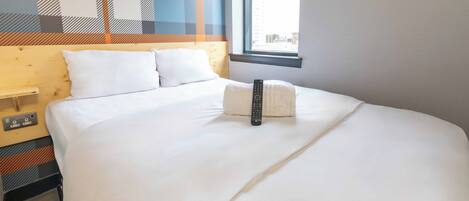 A hotel room with a large bed, a remote control, and a window with a city view.