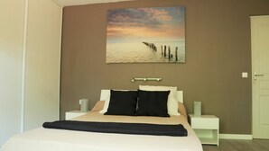 A bedroom with a bed, nightstands, a painting of a sunset over water, and a door.