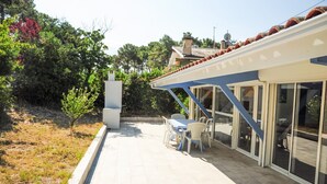 An outdoor patio with a table and chairs, a white column, and a glass door leading to a covered area.