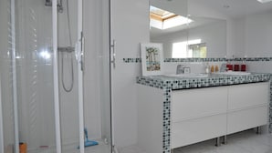 A modern bathroom with a glass shower enclosure, a white vanity with a tiled backsplash, and a large mirror above the sink.
