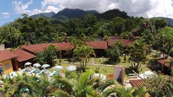Resort com vários edifícios, área de piscina com guarda-sóis e vegetação exuberante.