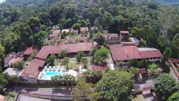 Vista aérea de um resort com vários edifícios, piscina e vegetação exuberante.
